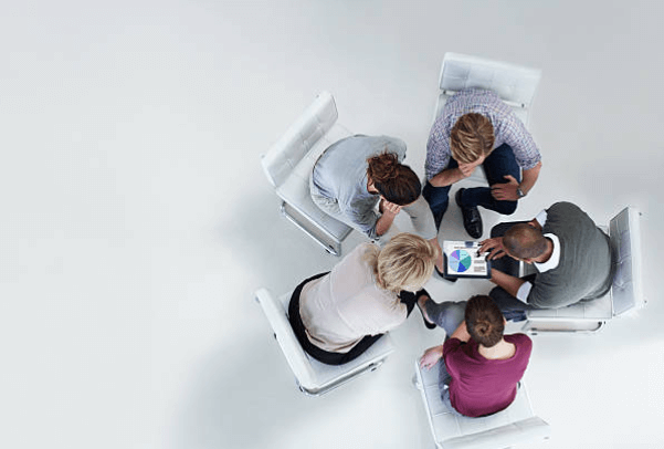 DMS4 - Aryo Systems A group of people sitting in a circle, collaborating and discussing a tablet displaying charts.