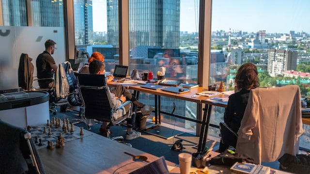 ant-rozetsky-HXOllTSwrpM-unsplash-2 - Aryo Systems Employees working at desks in a modern office with large windows overlooking a cityscape.